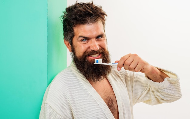 Photo homme se brosser les dents avec une brosse à dents et du dentifrice soins bucco-dentaires hygiène dentaire barbu en peignoir
