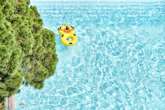 L'homme se détend sur des anneaux en caoutchouc gonflables dans la piscine avec de l'eau bleue claire