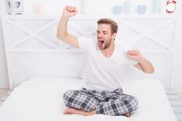 L'homme se détend au lit. matin parfait. bâiller et s'étirer le matin. se sentir douillet et confortable. Pyjama homme. Pyjama pour se détendre à la maison. homme somnolent. homme béant assis en pyjama.