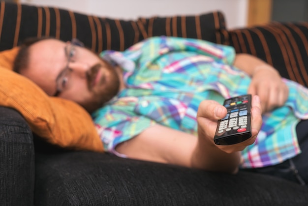 Homme se détendre dans un canapé avec télécommande en regardant la télévision.