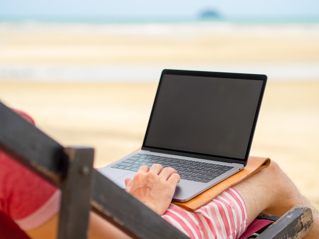 Homme se détendre sur le lit de camp et de travailler en ligne pendant les vacances à la plage en Thaïlande