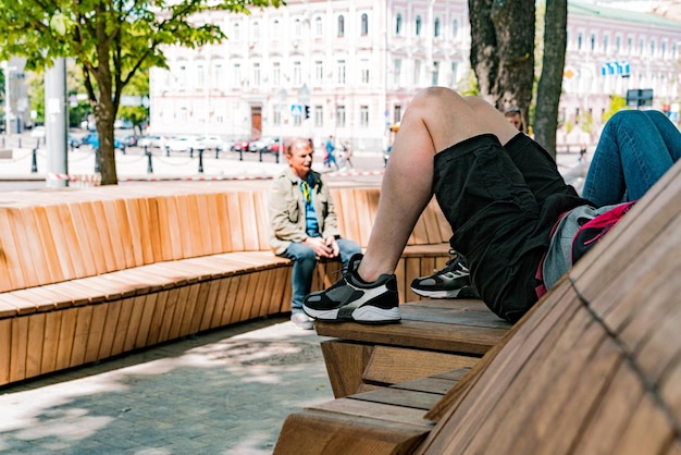 Homme se détendre sur un long banc en bois sur la place de la ville Géométrie confortable Marches ensoleillées marron en bois Perspective de jardinage Matériel paisible Marche Trottoir ScenicBig Plank Object Road