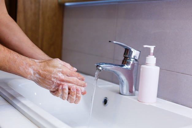 Homme se lavant les mains à l'eau courante, dans des toilettes publiques.