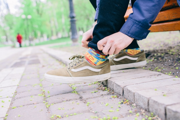 L'homme en se penche et en baskets s'asseoir sur un banc et attacher les lacets de chaussures. Seul dans le parc et à l'extérieur. Retrousser le bord du pantalon. Sois prêt.