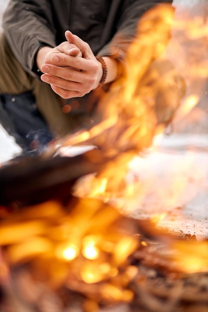 Homme se réchauffant les mains sur un feu de joie dans la nature en saison froide voyage d'hiver mode de vie photo aventure vacances actives en plein air camping extrême dans la forêt gelée enneigée seul gros plan sur les mains