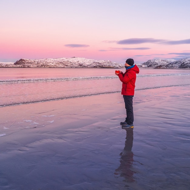 Un homme se réchauffe avec du thé. Thé chaud sur la côte arctique déserte et froide.