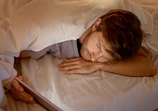 Homme se relaxant au lit sur une tablette numérique naviguant sur les réseaux sociaux ou en réseau sur Internet