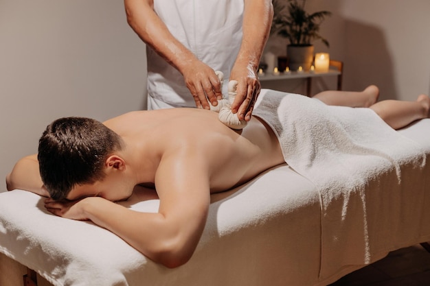 Homme se relaxant pendant le massage traditionnel thaïlandais aux herbes médecine orientale avec des sacs aromatiques soins du corps