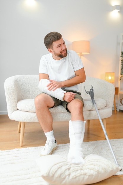 Photo homme se remettant d'une fracture d'accident blessure osseuse cassée avec des attelles pour les jambes, des attelles pour le cou, des attelles pour le col, des attelles pour le bras, un bras de soutien dans le salon, concept de sécurité sociale et d'assurance maladie