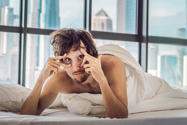 L'homme se réveille le matin dans un appartement du centre-ville avec vue sur les gratte-ciel. La vie dans le bruit du concept de grande ville. Pas assez de sommeil