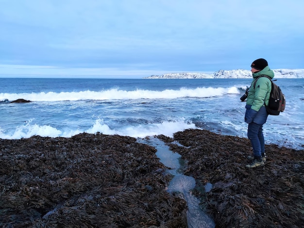 L'homme se tient au bord d'une mer froide. Un voyageur avec un appareil photo sur le fond de l'océan Arctique.