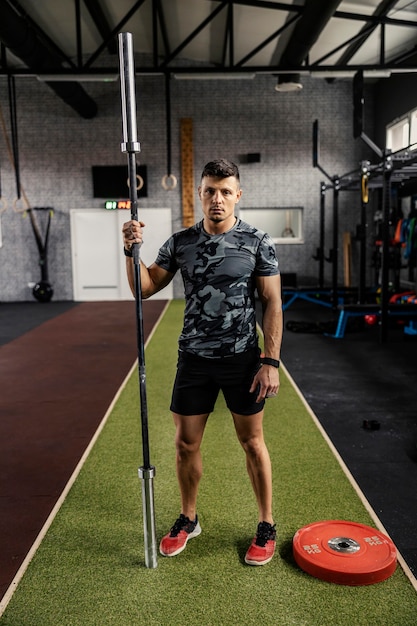 L'homme se tient au milieu de la salle de sport et tient une barre dans une main tout en posant