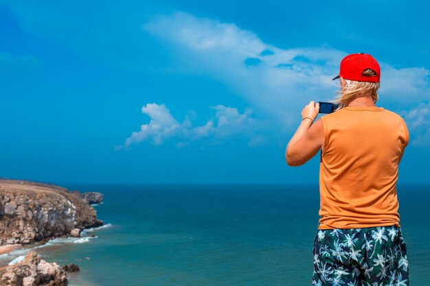 Photo un homme se tient au sommet d'une montagne et filme la mer et les montagnes avec sa caméra voyage et