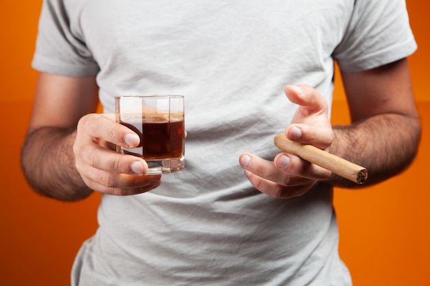 Un homme se tient avec un cigare et un verre de whisky