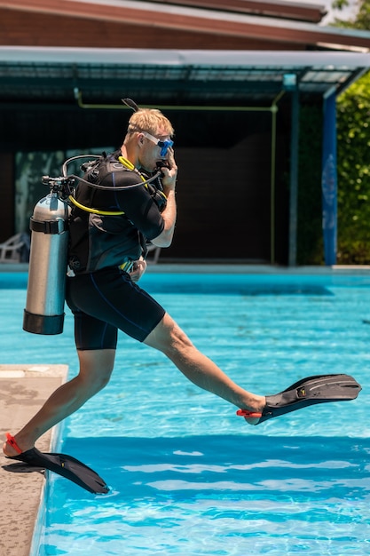 Un homme se tient dans un équipement de plongée et est prêt à plonger sous l'eau dans la piscine