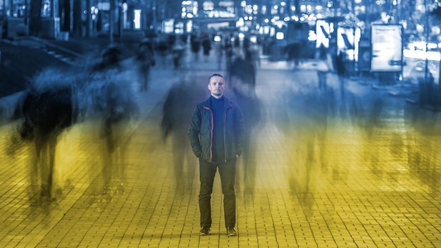 L'homme se tient dans la rue avec un flux de foule le soir la nuit