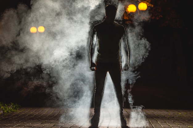 L'homme se tient dans la rue sombre sur fond de fumée. la nuit