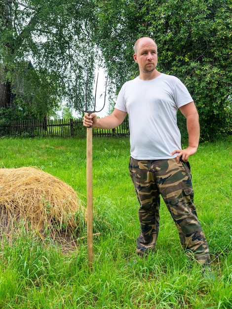 Un homme se tient dos à la caméra avec une fourche devant une botte de foin Paysage rural préparation d'aliments pour animaux Vie rurale Photo verticale