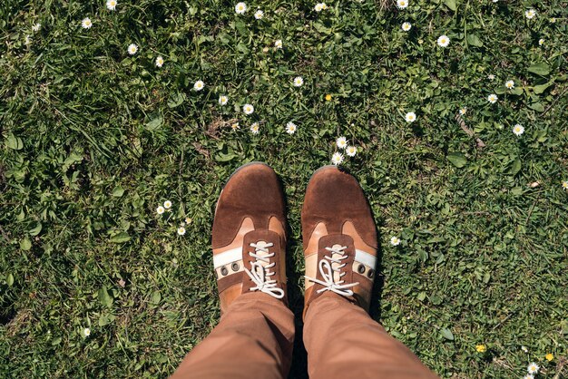 L'homme se tient sur la pelouse en baskets marron, formateurs. Première personne. Vue de dessus