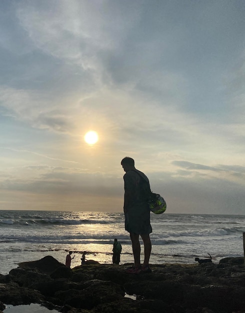 Un homme se tient sur une plage devant un coucher de soleil avec un panneau qui dit "plage".