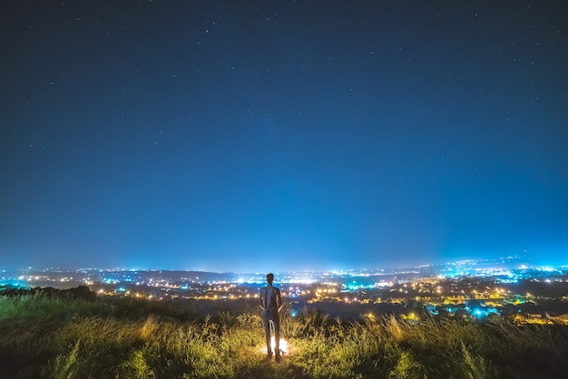 L'homme se tient près du feu de joie sur le fond des lumières de la ville. la nuit