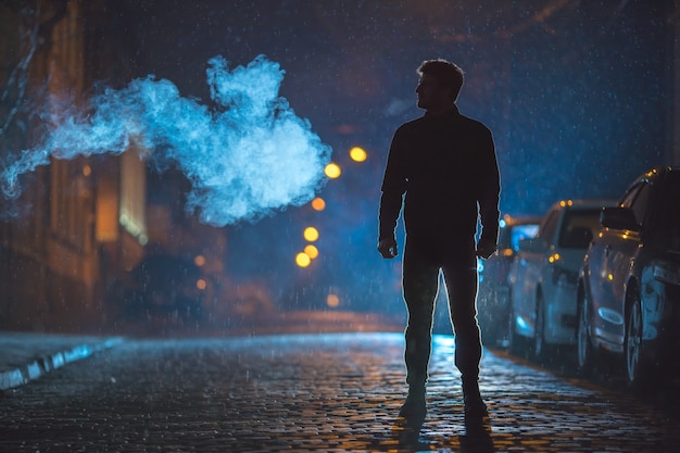 L'homme se tient près de la fumée. Le soir la nuit. Prise de vue au téléobjectif