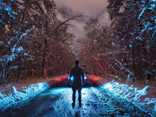 L'homme se tient sur la route forestière près de la voiture. le soir la nuit