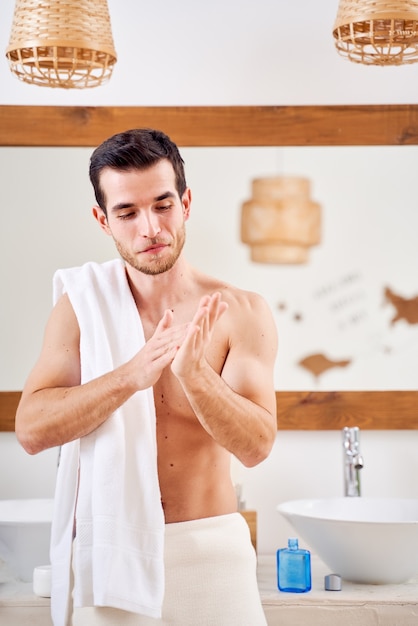 L'homme se tient avec une serviette sur ses épaules devant le miroir de la salle de bain