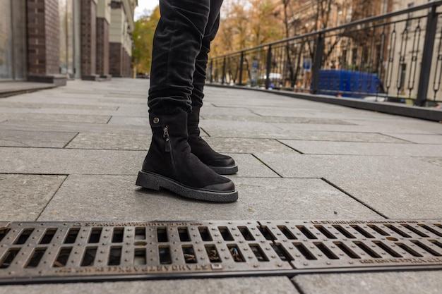 Un homme se tient sur un trottoir portant des bottes noires.