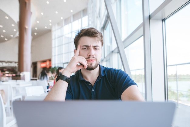 Homme séduisant avec une barbe de sydt dans un café et concentré sur l'écran d'un ordinateur portable.