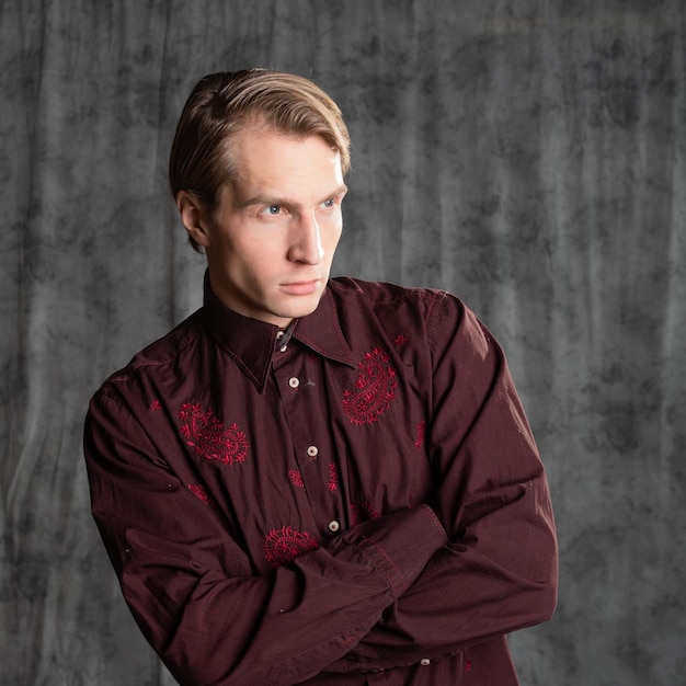 Un homme séduisant dans un élégant costume chemise bordeaux avec broderie photo en studio sur un ba gris