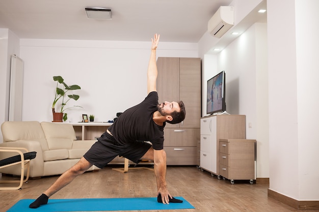 Homme séduisant essayant des poses de yoga côté étendu sur le sol de sa maison. Entraînement athlétique.