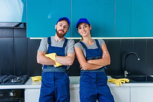 Homme séduisant et jolie femme en vêtements de travail posant sur l'appareil photo dans la cuisine contemporaine avec des détergents