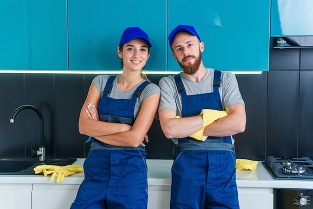 Homme séduisant et jolie femme en vêtements de travail posant sur l'appareil photo dans la cuisine contemporaine avec des détergents