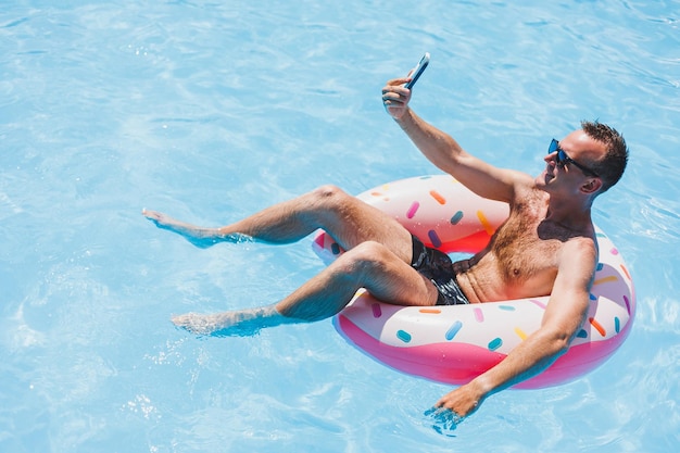 Un homme séduisant se détend sur un anneau gonflable dans la piscine Un homme dans la piscine parle au téléphone vacances et concept de temps libre