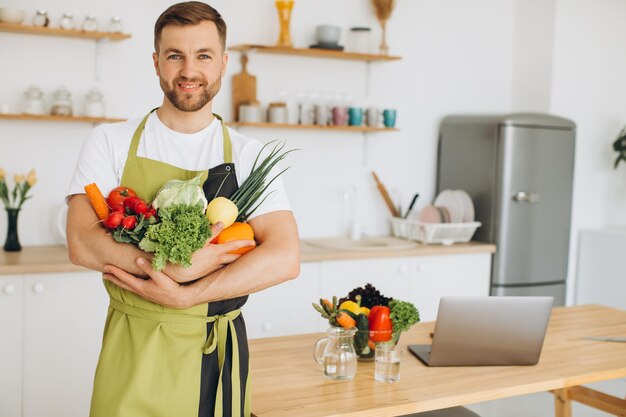 Homme séduisant tenant de nombreux légumes frais différents dans la cuisine à la maison