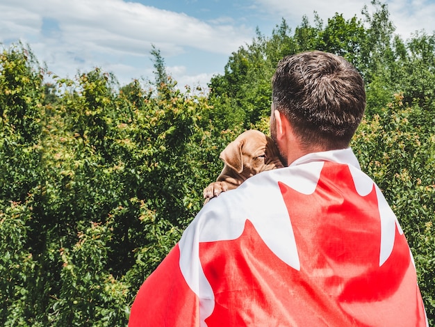 Un homme séduisant tient un charmant chiot sur fond de ciel bleu par une journée claire et ensoleillée. Extérieur, gros plan. Concept de fête nationale