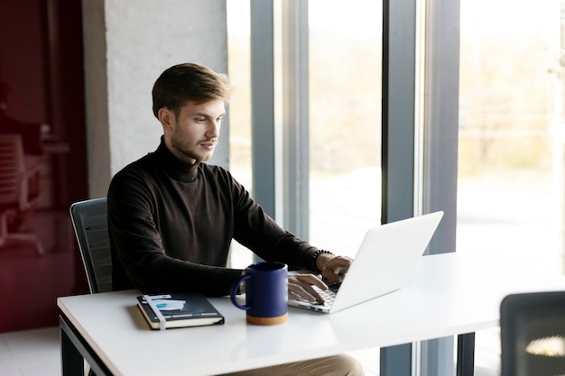 Homme séduisant travaillant sur ordinateur portable dans un bureau moderne