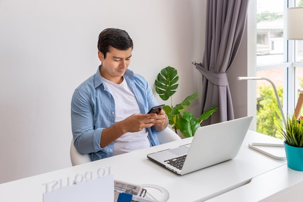 Un homme séduisant travaille à la maison avec un ordinateur portable et utilise un téléphone portable