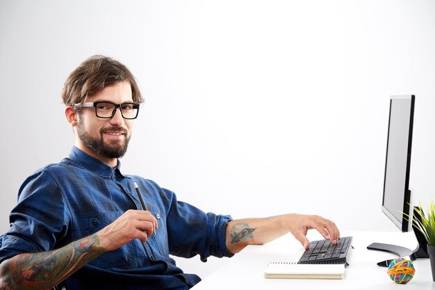 Homme séduisant vêtu d'une chemise bleue assis avec ordinateur portable, concept indépendant, portrait, emploi en ligne, processus de travail, regardant la caméra.