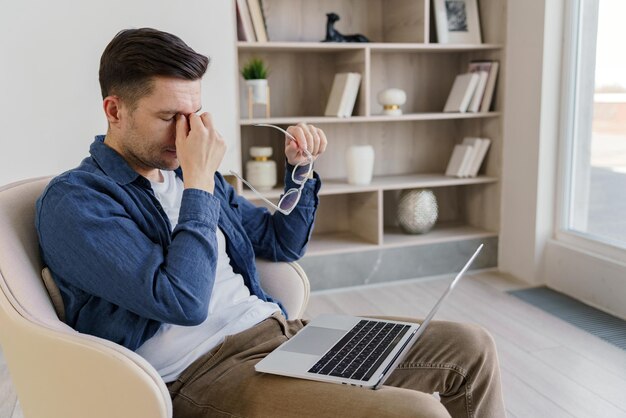 Un homme semble stressé ou fatigué prenant un moment tout en travaillant sur son ordinateur portable dans une maison sereine