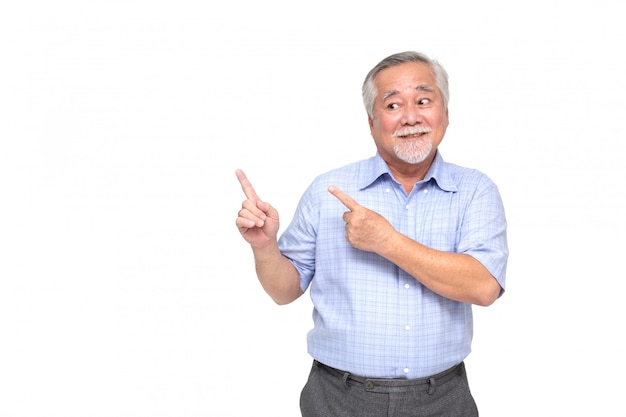 Homme senior asiatique souriant et pointant vers l'espace de copie vide isolé sur mur blanc