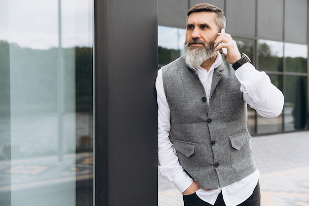 Un homme senior aux cheveux gris barbu utilise et parle sur un smartphone