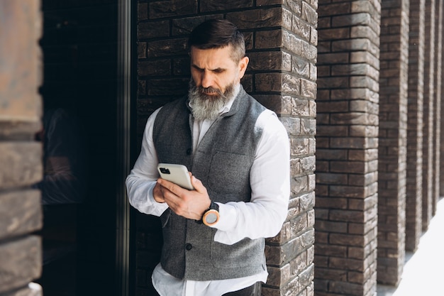 Un homme senior aux cheveux gris barbu utilise et parle sur un smartphone
