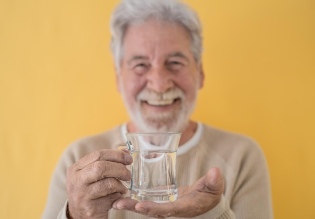 Homme senior barbu attrayant défocalisé tenant un verre d'eau fraîche regardant la caméra debout sur fond jaune