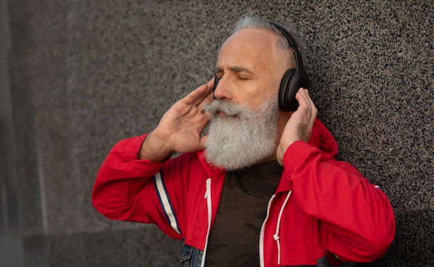 Un homme senior barbu branché, écouter de la musique en plein air. Homme mature de mode.