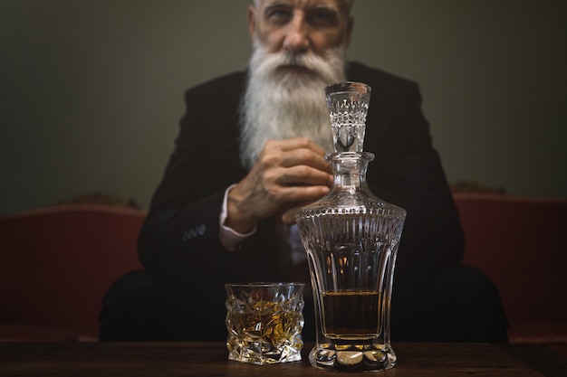 Homme senior barbu élégant et beau buvant du whisky