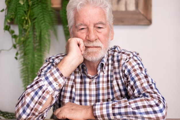 Homme senior barbu sérieux avec la main sur le visage regardant vers le bas perdu dans ses pensées assis à table de café