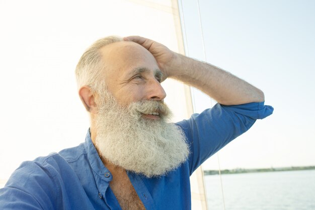 Homme senior barbu sur voilier ou yacht flottant sur le lac.