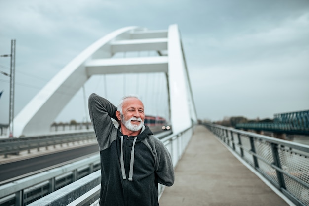 Homme senior en bonne forme physique qui s&#39;étend sur le pont de la ville.